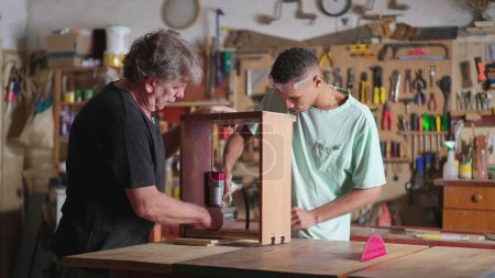 Foto de Carpintero mayor y joven aprendiz colaborando en taller de carpintería - Imagen libre de derechos