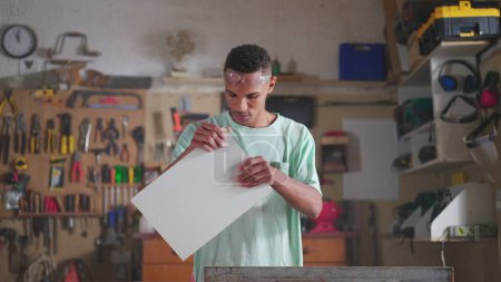 Foto de Un joven carpintero brasileño negro concentrado dedicado al trabajo de taller, aserrado de madera con máquina industrial. Persona dedicada a la ocupación laboral - Imagen libre de derechos
