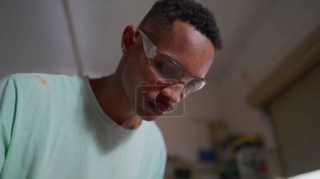 Téléchargez les photos : One Focused Young Black Carpenter Trimming Wood at Workshop. Machine d'exploitation d'employé concentré pour façonner le bois - en image libre de droit