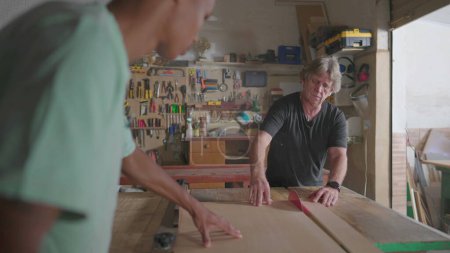 Foto de Maestro carpintero cortando madera con la máquina de sierra con la ayuda de su asistente. Trabajos de carpintería en carpintería local, producción industrial. Trabajo de profesión - Imagen libre de derechos