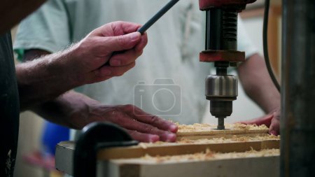 Foto de Un joven trabajador brasileño negro utilizando la máquina de perforación para agujero masculino en la superficie de madera en el taller de carpintería - Imagen libre de derechos