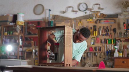Foto de Un carpintero negro concentrado usando equipo de perforación en taller de carpintería - Imagen libre de derechos