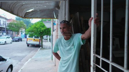 Foto de Pensativo carpintero brasileño tomando una pausa del trabajo, de pie fuera de la tienda local - Imagen libre de derechos