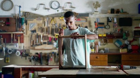 Téléchargez les photos : Un jeune menuisier brésilien noir engagé dans la fabrication de meubles de construction de travail à l'atelier - en image libre de droit