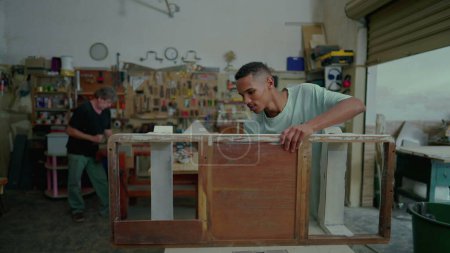 Téléchargez les photos : Jeune employé de menuiserie atelier polissage morceau de meubles en bois, la réparation et la rénovation de vieux objets. Occupation d'un emploi dans une petite entreprise - en image libre de droit