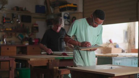 Foto de Candid Carpentry Workshop Scene of Master Carpenter and Apprentice at Work (en inglés). Trabajadores concentrados dedicados a la ocupación laboral - Imagen libre de derechos