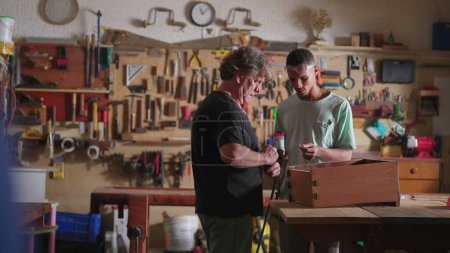 Foto de Escena franca del carpintero senior y del joven aprendiz junior que trabaja en el taller de carpintería - Imagen libre de derechos