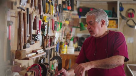 Foto de Hombre mayor organizando herramientas colgando en la pared en taller carpintería - Imagen libre de derechos