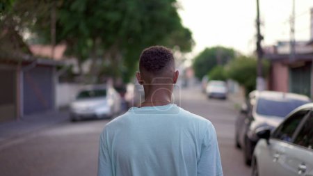 Téléchargez les photos : Arrière d'un jeune homme noir marchant dans la rue. Une personne afro-américaine se promène dans un environnement urbain. Concept de parcours de vie - en image libre de droit