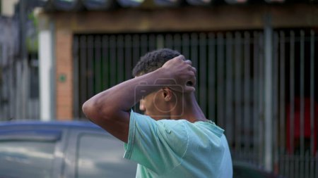 Foto de Un joven brasileño negro pensativo preocupado por la vida mientras camina por la calle urbana. Persona afroamericana ansiosa que desciende paseando en ambiente urbano frotando cara y cuello - Imagen libre de derechos