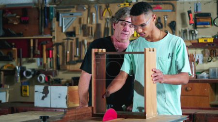 Photo for Master carpenter guiding apprentice at carpentry workshop, boss teaching student with woodwork using saw machine to slice piece of wood, industry job - Royalty Free Image