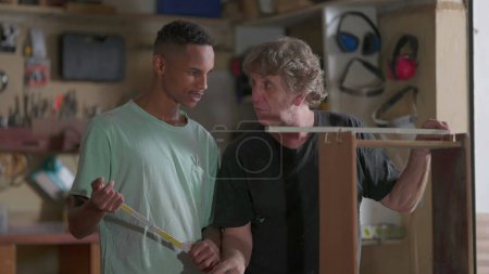 Photo for Master carpenter teaching apprentice the process of furniture building and repair at carpentry workshop, measuring piece of wood with ruler - Royalty Free Image