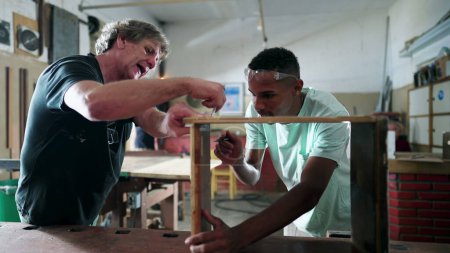 Foto de Maestro carpintero guiando a un joven aprendiz negro en el taller de carpintería, personas comprometidas con su ocupación laboral, trabajo en la industria, trabajando con sus manos. Los brasileños en el trabajo - Imagen libre de derechos