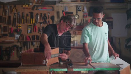 Téléchargez les photos : Atelier de menuiserie de maître menuisier et apprenti mesurant le bois avec règle, engagé dans la construction et la réparation de meubles - en image libre de droit