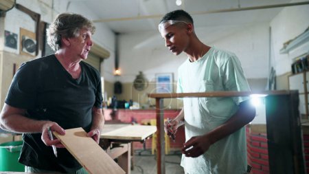 Photo for Master carpenter guiding a young black apprentice at carpentry workshop, people engaged with their job occupation, industry job, working with their hands. Brazilian people at work - Royalty Free Image