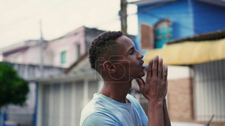 Téléchargez les photos : Religieux homme noir sud-américain priant Dieu dans la rue urbaine, fidèle brésilien regardant vers le haut pour le soutien divin - en image libre de droit