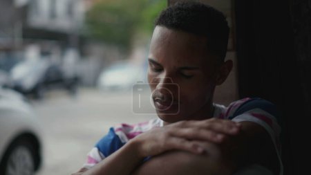 Téléchargez les photos : Un jeune homme noir déprimé lutte contre l'isolement social et la maladie mentale, couvrant son visage de honte et de regret. Personne d'ascendance afro-américaine face au désespoir tranquille - en image libre de droit