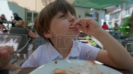 Téléchargez les photos : Jeune amant de pizza scène de petit garçon relâchant une tranche dans un cadre de restaurant - en image libre de droit