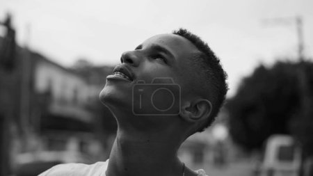 Photo for One faithful African American man looking up at sky with HOPE. Smiling joyful young person gazing upwards in monochromatic black and white - Royalty Free Image