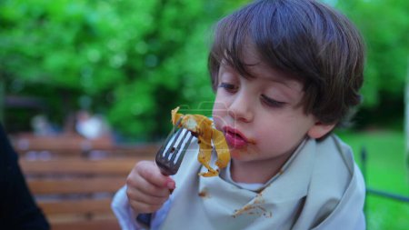 Téléchargez les photos : Petit garçon désordonné mangeant des pâtes pour le déjeuner en plein air dans un cadre ensoleillé. Portrait en gros plan de nouilles savoureuses pour enfants - en image libre de droit