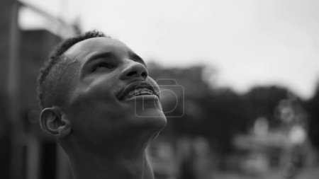Photo for One faithful African American man looking up at sky with HOPE. Smiling joyful young person gazing upwards in monochromatic black and white - Royalty Free Image