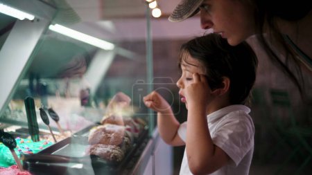 Téléchargez les photos : Petit garçon pointant vers la saveur de la crème glacée, le choix du dessert derrière le comptoir en verre - en image libre de droit