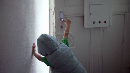Photo for Child opening front door of home and stepping out in street. One little boy's hand reaching door knob and opens residence entrance while wearing hoodie - Royalty Free Image