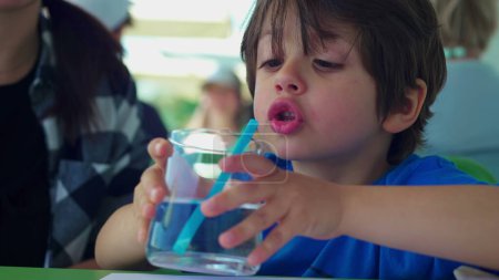 Téléchargez les photos : Petit garçon boire de l'eau avec de la paille au restaurant. Enfant gros plan visage hydratant lui-même pendant la journée d'été - en image libre de droit