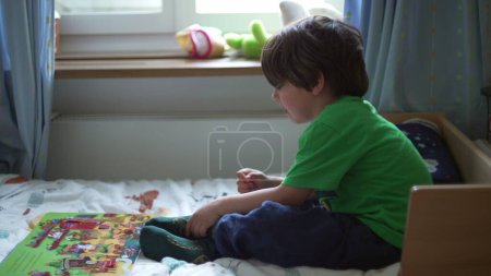 Téléchargez les photos : Petit garçon bouleversé luttant pour mettre des chaussettes dans la chambre. Frustré gamin essayé de mettre des vêtements lui-même - en image libre de droit
