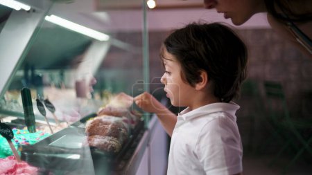 Téléchargez les photos : Petit garçon pointant vers la saveur de la crème glacée, le choix du dessert derrière le comptoir en verre - en image libre de droit