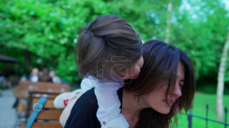 Téléchargez les photos : Petit garçon abrasif grimpant durement sur le cou de la mère, montrant peu d'inquiétude à l'émotion de maman en plein air à l'extérieur. parent dans l'inconfort, concept parental - en image libre de droit