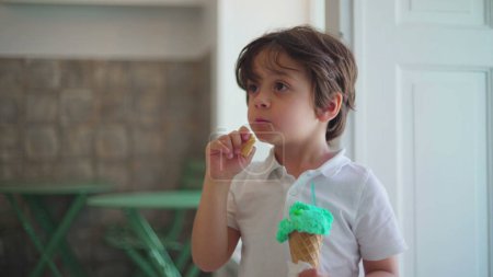 Téléchargez les photos : Enfant tenant cône coloré de crème glacée au magasin de salon. Enfant authentique mangeant des desserts sucrés - en image libre de droit