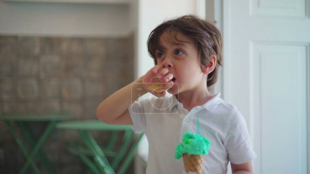 Foto de Niño sosteniendo colorido cono de helado en la tienda de salón. Auténtico niño comiendo dulce postre alimentos - Imagen libre de derechos