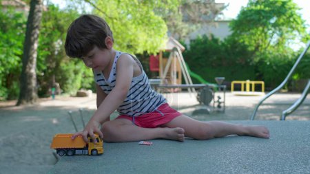 Foto de Niño feliz juega con camión de juguete afuera en el parque en el soleado día de verano. Niño juguetón absorto en su propio mundo creativo - Imagen libre de derechos