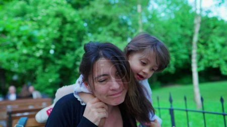 Photo for Abrasive little boy climbing on top of mother's neck harshly, showing little concern to mom's emotion in open air outside. parent in discomfort, parenting concept - Royalty Free Image