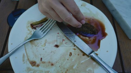 Hand dipping piece of bread into sauce in empty plate, dining aftermath leftovers