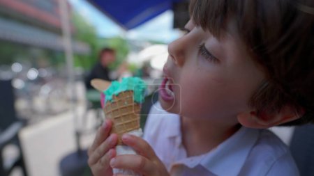 Téléchargez les photos : Enfance Bliss scène de concentré jeune garçon jouit coloré glace-crème cône en été la lumière du soleil - en image libre de droit