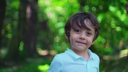 Téléchargez les photos : Portrait de parc de jour lumineux / Caméra de visages de petit garçon au milieu de verdure luxuriante - en image libre de droit