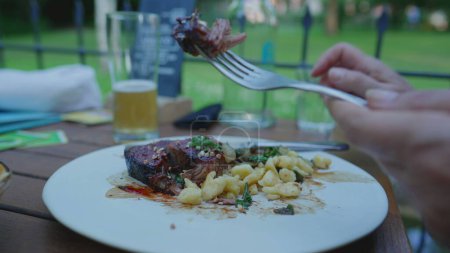 Foto de Primer plano de corte a mano y comer carne y pasta en el plato en el restaurante de lujo, plato groumet en el lugar al aire libre - Imagen libre de derechos