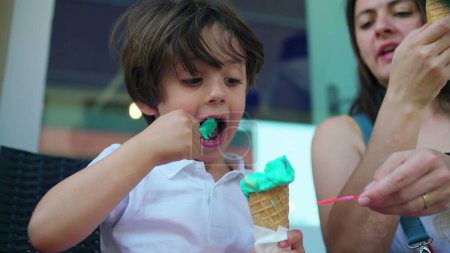 Photo for Child eating colorful ice-cream cone with mom outside. One caucasian little boy enjoys sweet dessert during summer day - Royalty Free Image
