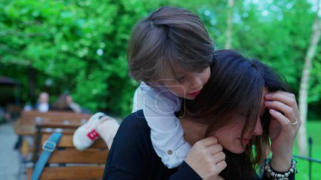 Photo for Abrasive little boy climbing on top of mother's neck harshly, showing little concern to mom's emotion in open air outside. parent in discomfort, parenting concept - Royalty Free Image