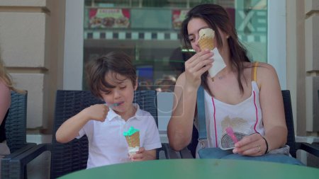 Photo for Happy mother and child enjoying ice-cream cone outside at parlor shop. Mom and son eating and savoring sweet dessert treat, smiling expression - Royalty Free Image