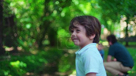 Téléchargez les photos : Portrait d'un petit garçon au parc pendant une journée ensoleillée. Après-midi d'été vert vif, gros plan du visage de l'enfant se tournant vers la caméra - en image libre de droit