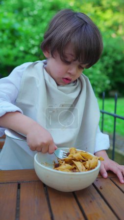 Foto de Little Boy Savoring Pasta, Camisa blindada con servilleta para la limpieza, Vídeo vertical - Imagen libre de derechos