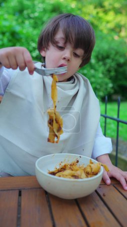Photo for Little Boy Savoring Pasta, Shirt Shielded with Napkin for Cleanliness, Vertical Video - Royalty Free Image
