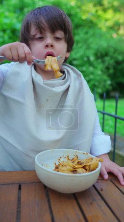 Téléchargez les photos : Pâtes alimentaires pour petit garçon, Chemise blindée avec serviette pour la propreté, Vidéo verticale - en image libre de droit