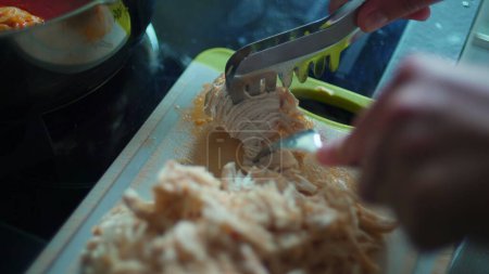 Photo for Shredding pieces of chicken with fork, close-up hand preparing food meal - Royalty Free Image