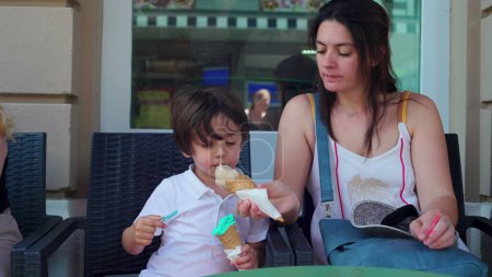 Photo for Mother sharing ice-cream cone to son for him to try a different taste. Parent and child enjoying sweet treat, savoring summer food dessert - Royalty Free Image