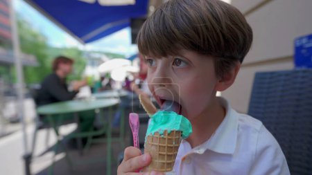 Photo for Little Boy Savors Ice-Cream cone on a Summer Day. Child licking colorful blue icecream outside - Royalty Free Image