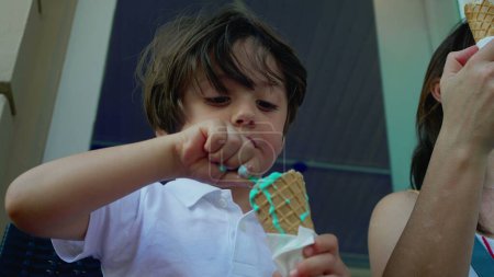 Photo for Concentrated small boy savoring colorful blue ice-cream cone at parlor outside during summer day, close-up of a caucasian male child eating sweet dessert - Royalty Free Image